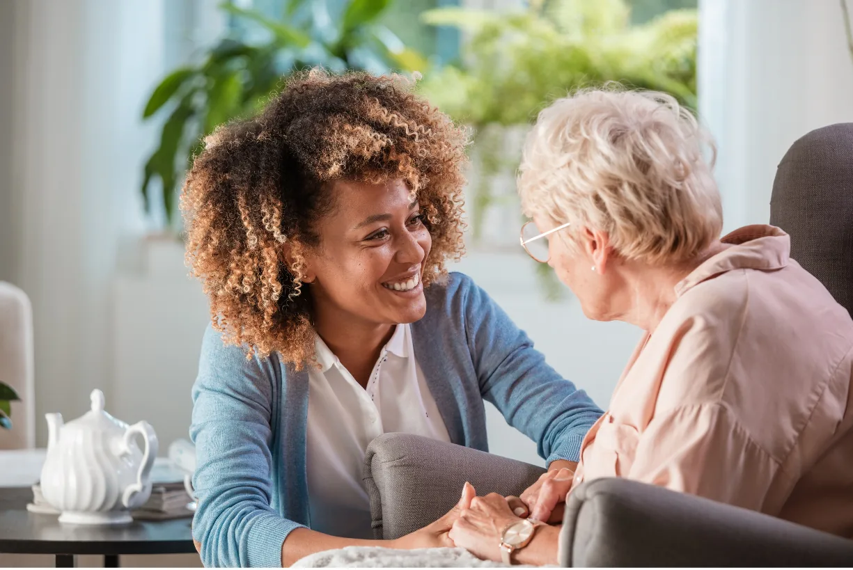 A carer holding an older woman's hand as they talk together